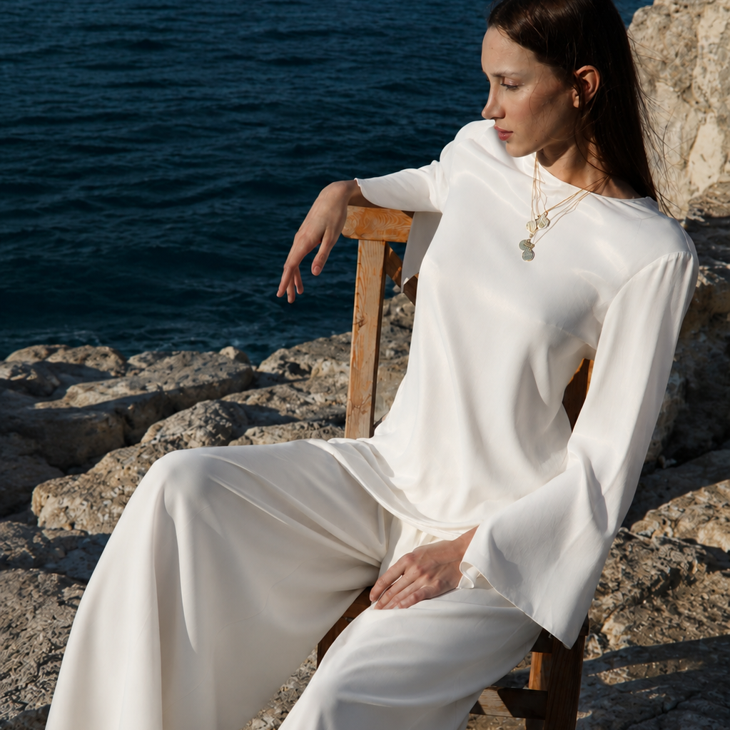 Woman in a white dress sitting on a chair by the ocean.