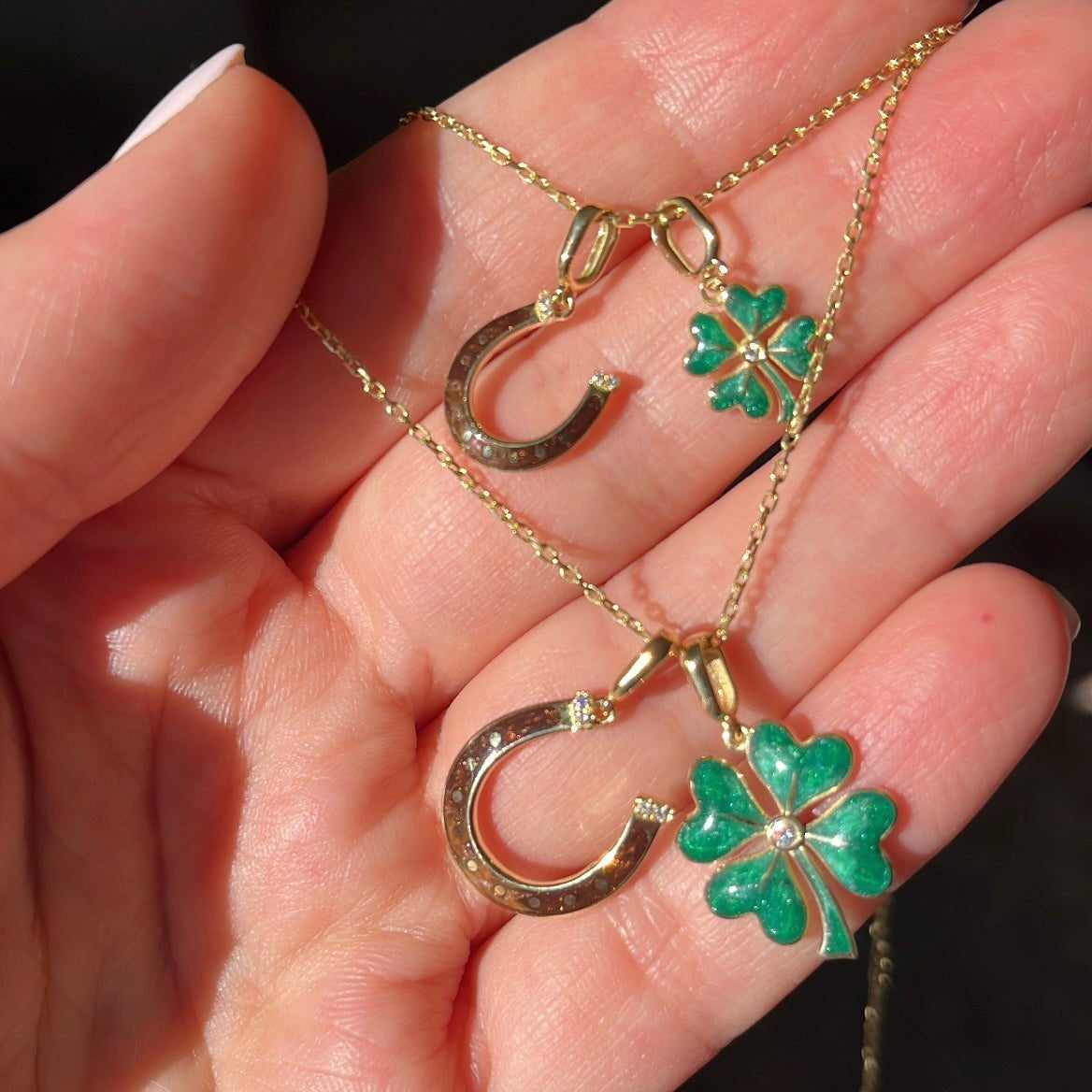 Gold necklace with clover and horseshoe pendants held in a hand against a dark background