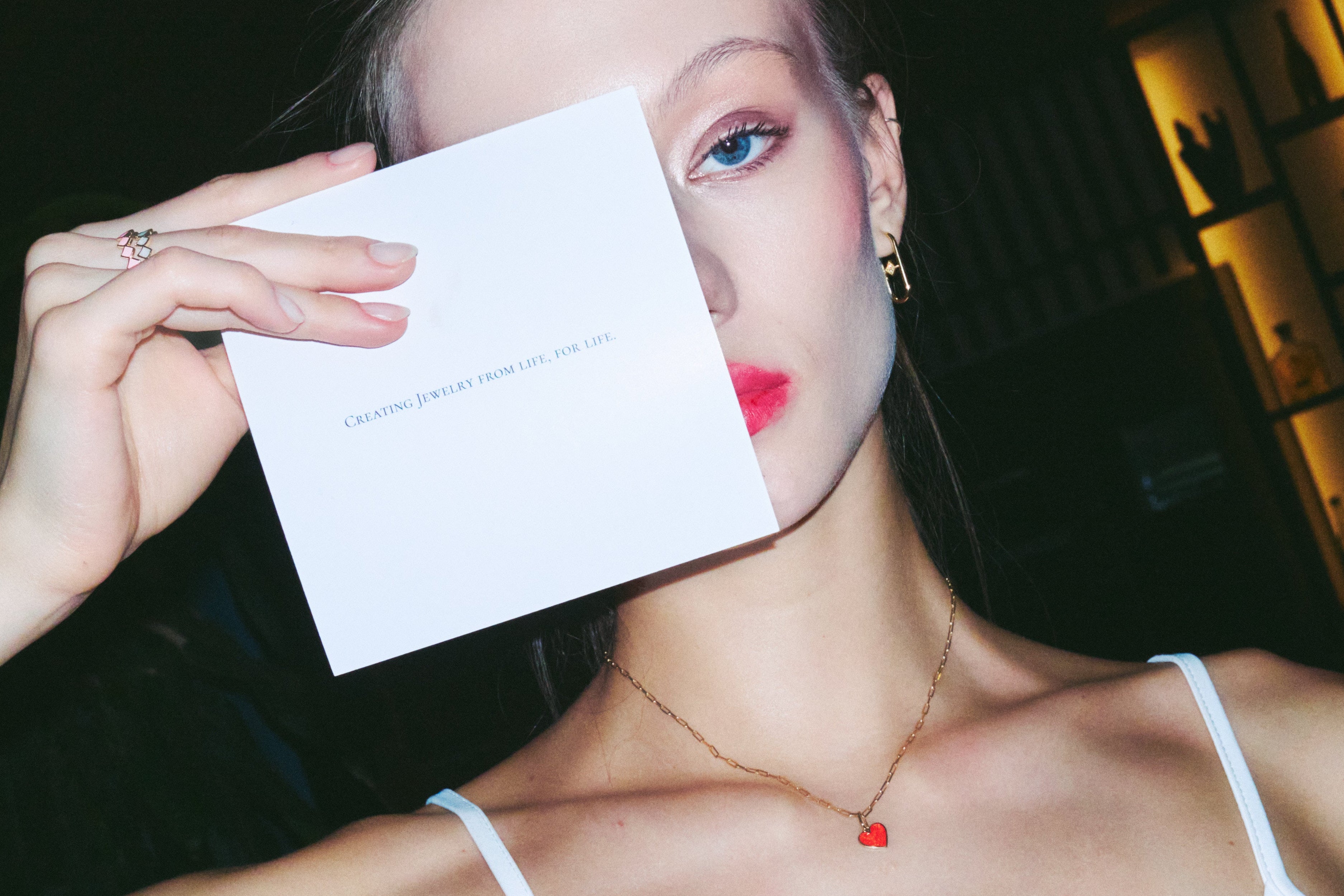Woman holding a piece of paper over her face in a dimly lit room.
