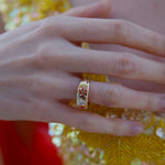 Close-up of a hand wearing a colorful ring with a yellow sequined garment in the background.