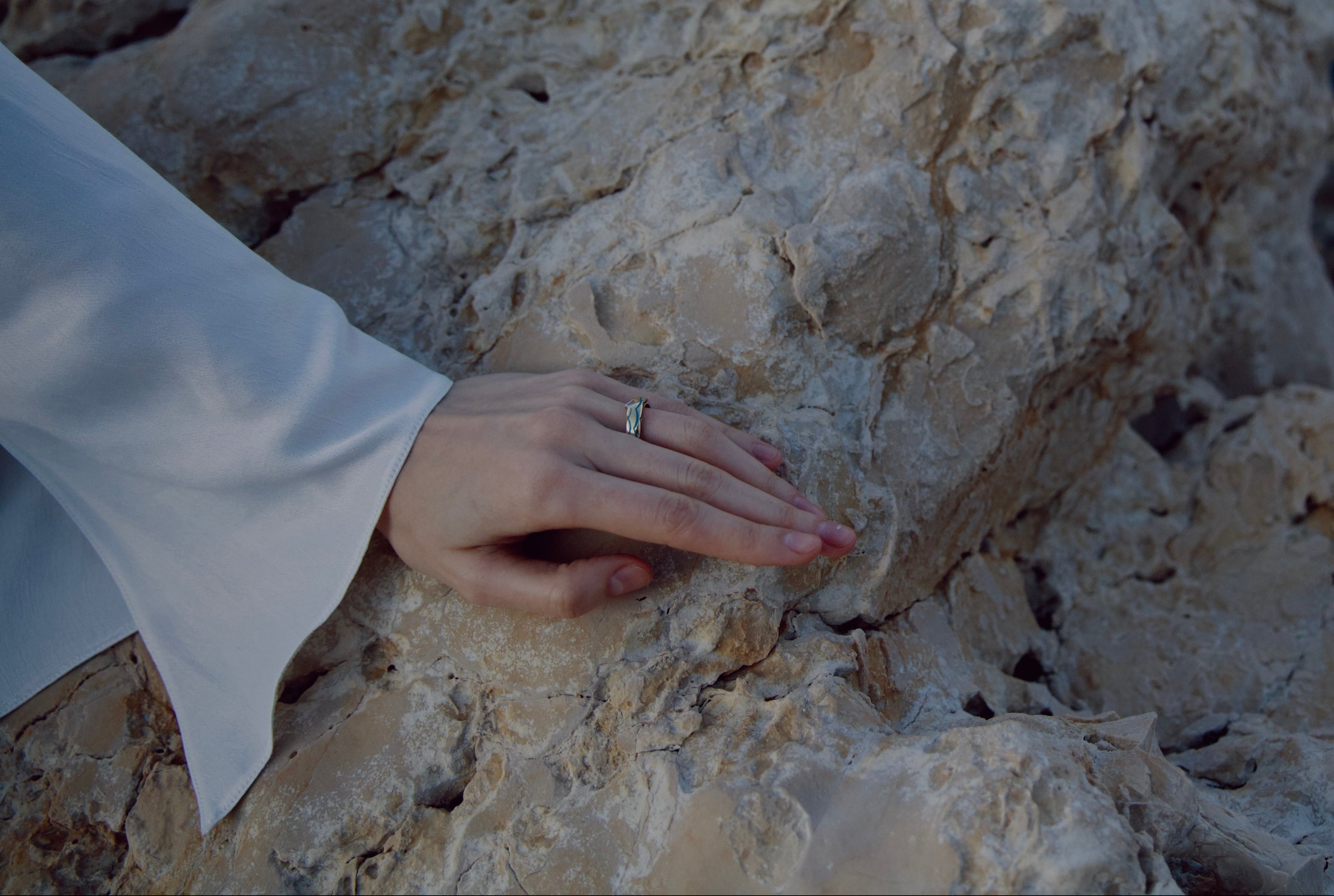 Hand touching a textured rock with ocean waves in the background